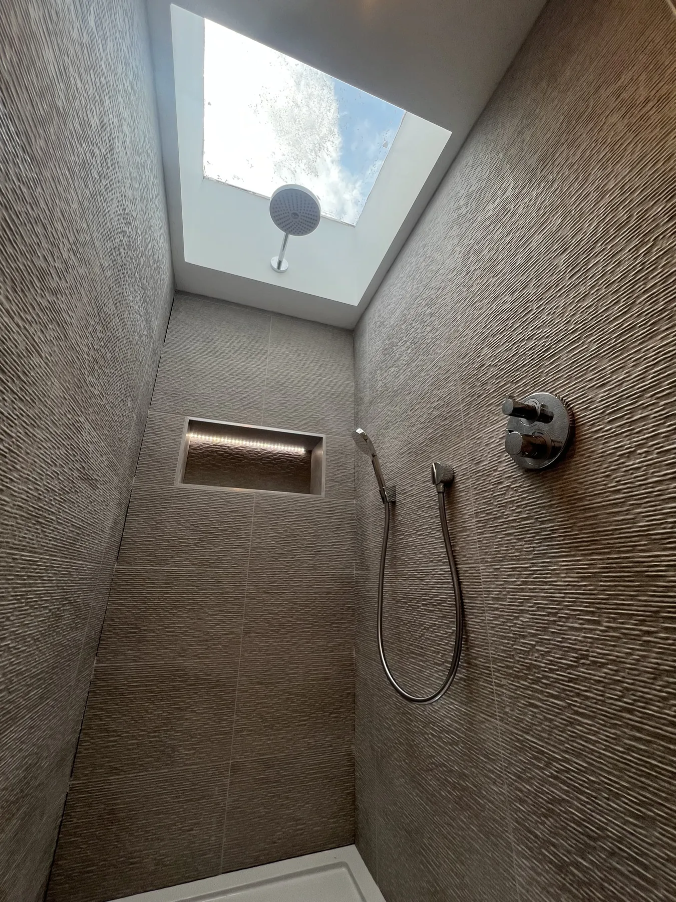 Textured tiled shower beneath a skylight